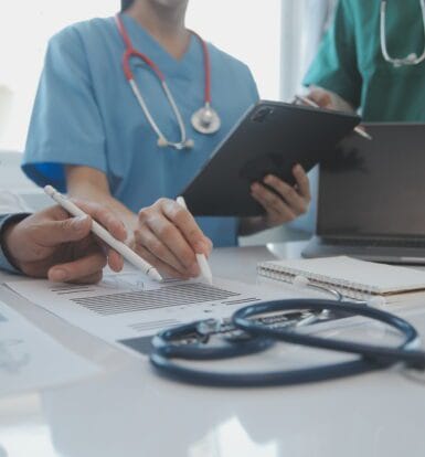 A medical scribe documenting patient information while a physician interacts with a patient.