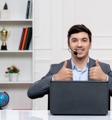 A smiling virtual assistant wearing a headset, sitting at a desk with a laptop and giving thumbs up, showcasing professional support.