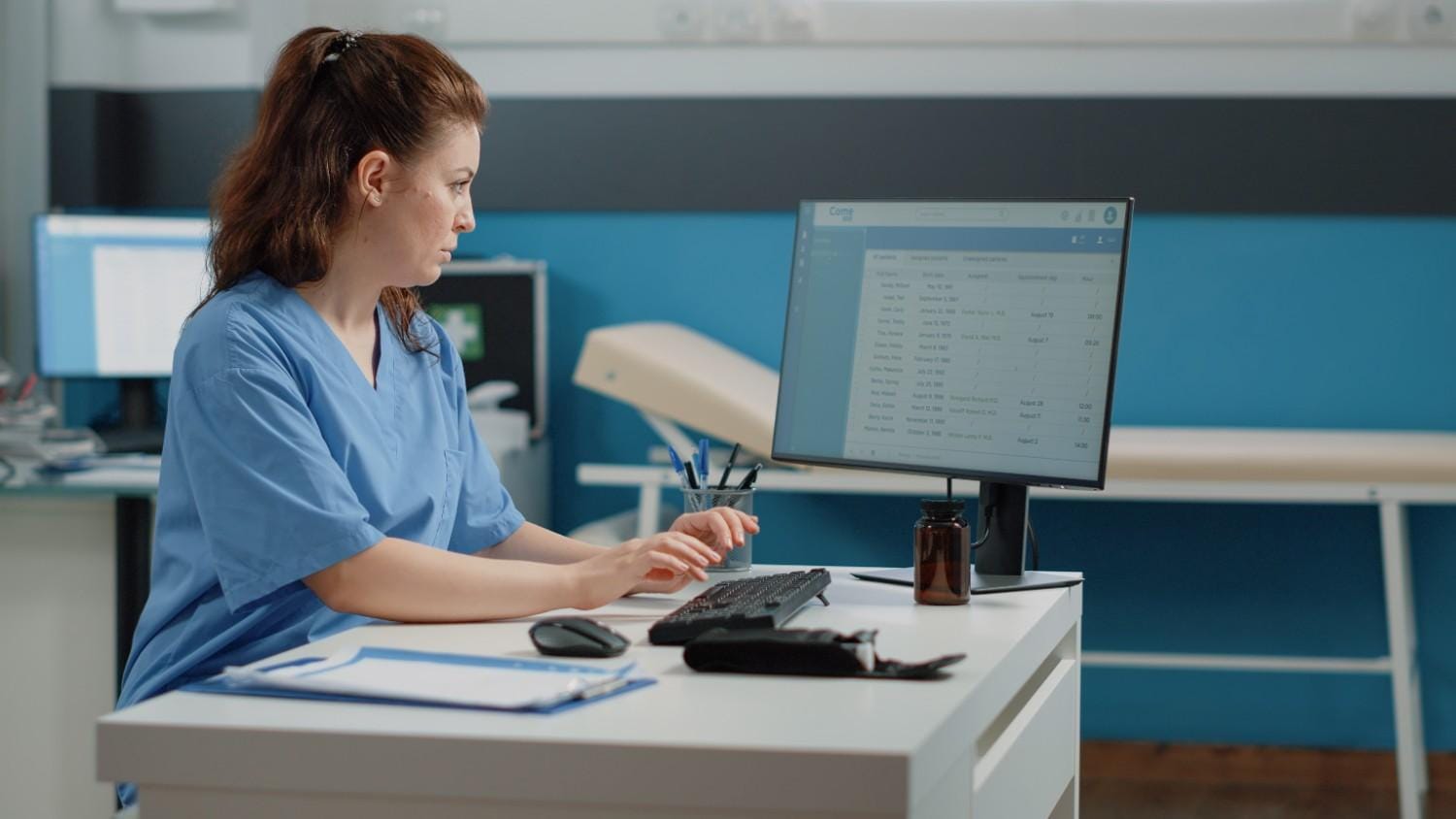 Healthcare professional in scrubs working on a computer for insurance verification and medical data entry.