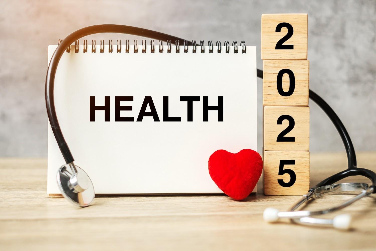 Notebook displaying the word "HEALTH" with a stethoscope, heart, and wooden blocks reading "2025," symbolizing advancements in healthcare.