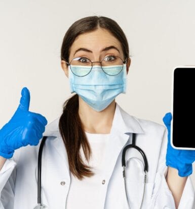 A smiling healthcare professional wearing a mask and gloves holding a smartphone, symbolizing mobile marketing in healthcare.