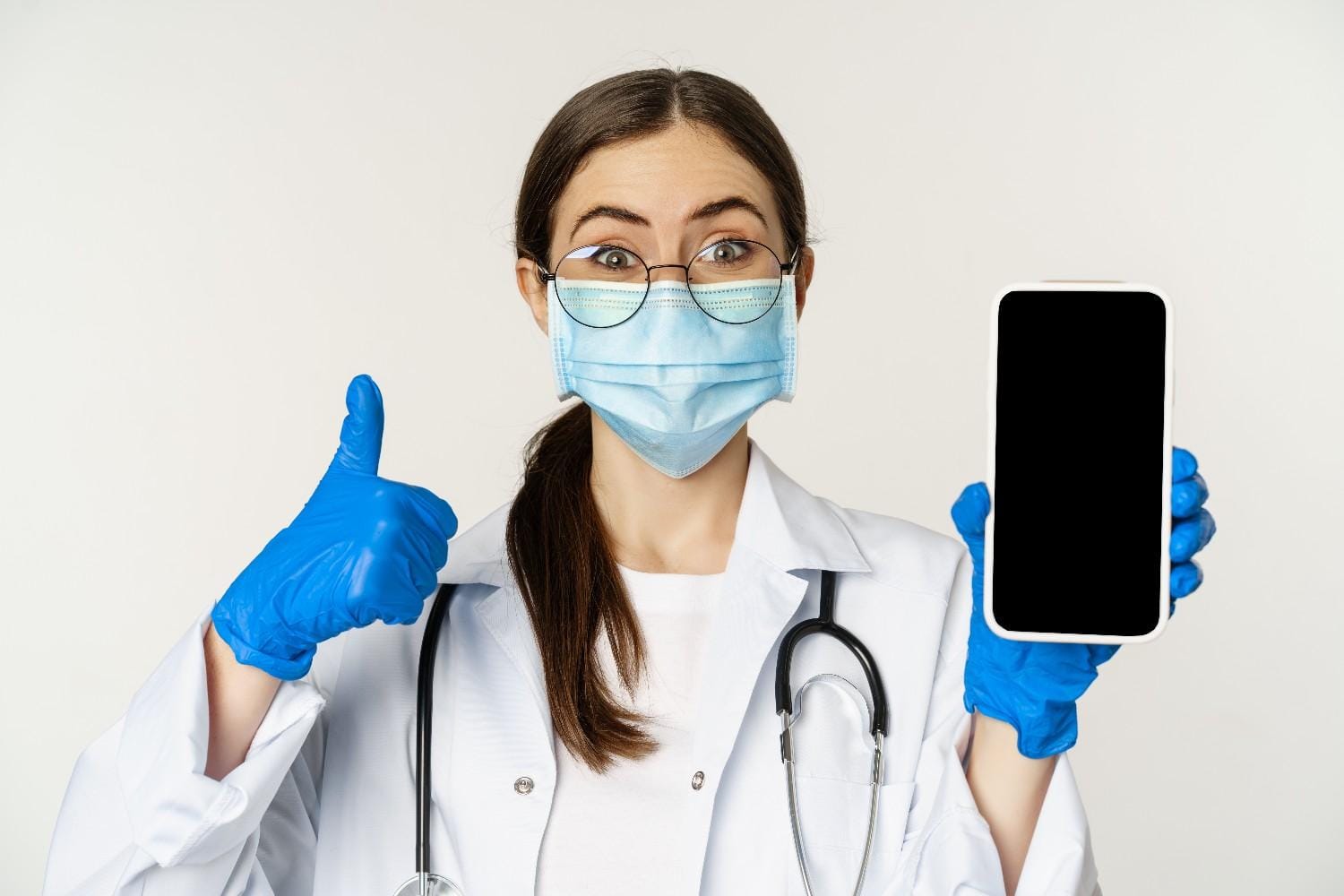 A smiling healthcare professional wearing a mask and gloves holding a smartphone, symbolizing mobile marketing in healthcare.