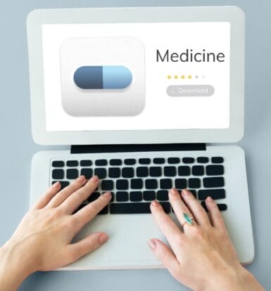 Hands typing on a laptop displaying a medicine review with star ratings and a download button, symbolizing online reviews in healthcare.