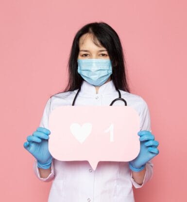 A healthcare professional wearing a mask and gloves holding a social media like icon