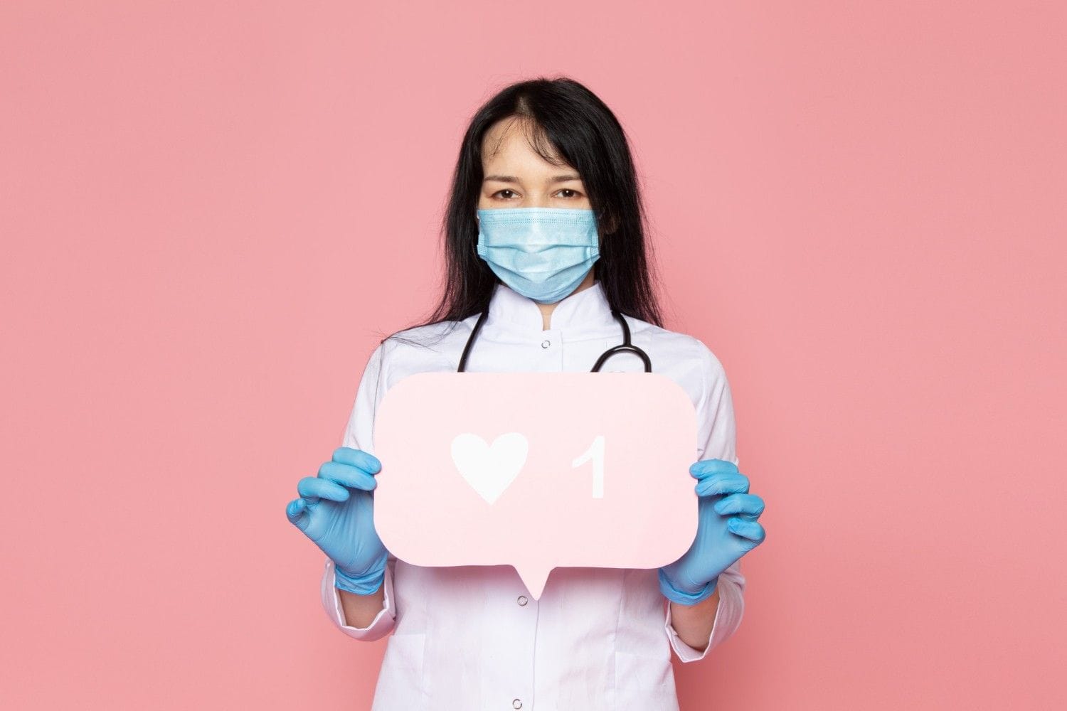 A healthcare professional wearing a mask and gloves holding a social media like icon