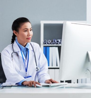 Doctor working in a modern healthcare setting, focused on a computer, demonstrating the integration of technology in medical practices.