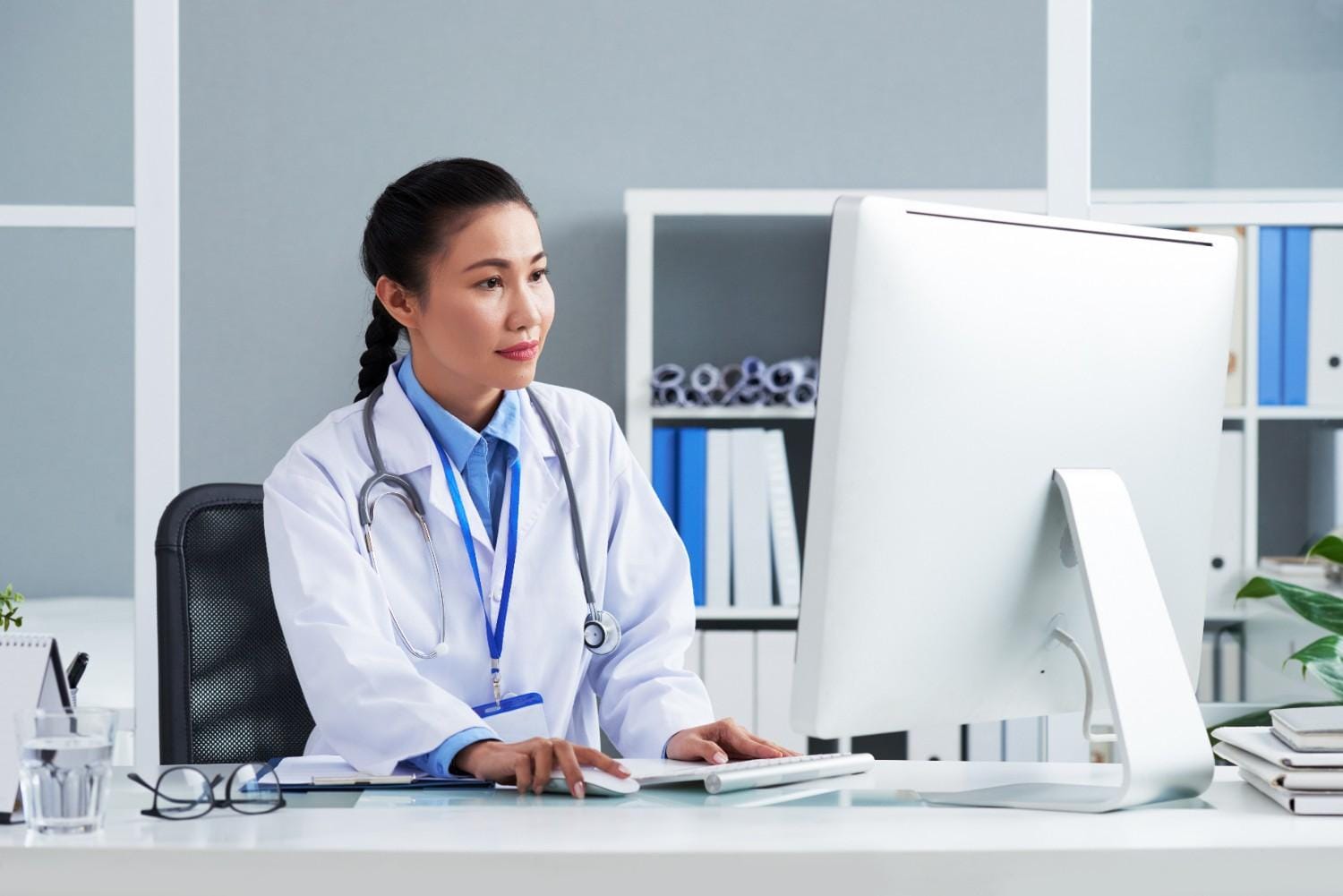 Doctor working in a modern healthcare setting, focused on a computer, demonstrating the integration of technology in medical practices.