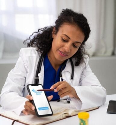 A female doctor using a mobile app for medical clinic appointment scheduling while reviewing notes in her office.