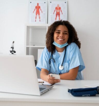 Smiling healthcare professional using a laptop and smartphone, showcasing the efficiency of Virtual Medical Assistants Healthcare services.