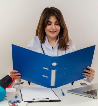 A healthcare professional reviewing a patient file for insurance verification at a desk with medical tools and a laptop.