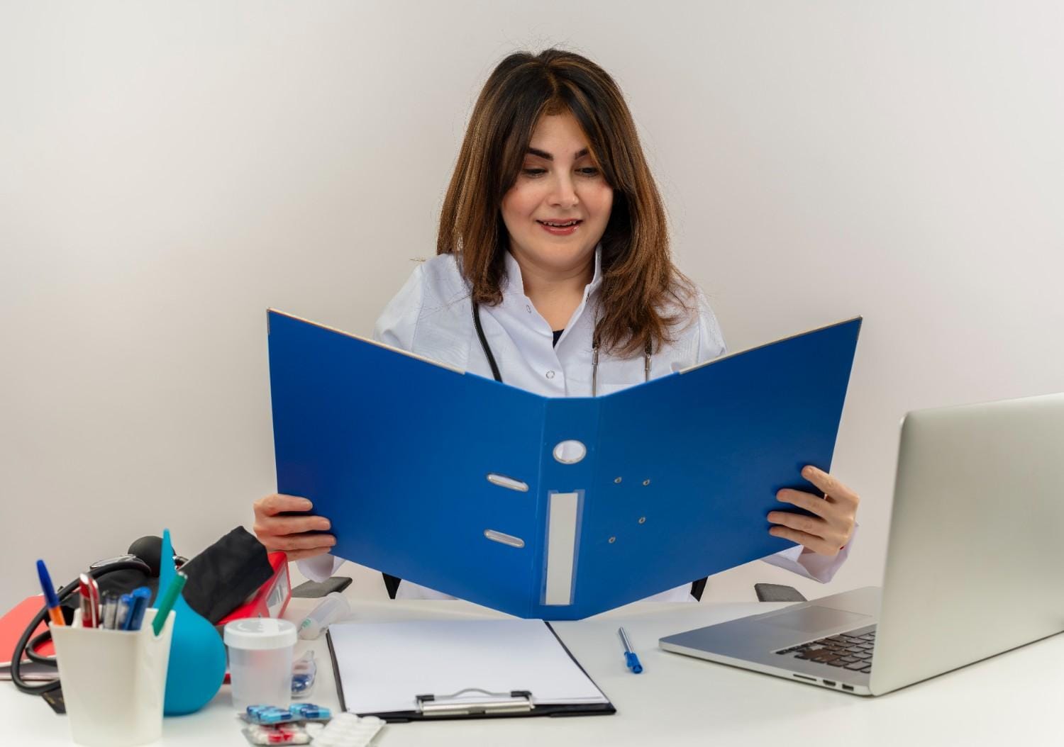 A healthcare professional reviewing a patient file for insurance verification at a desk with medical tools and a laptop.