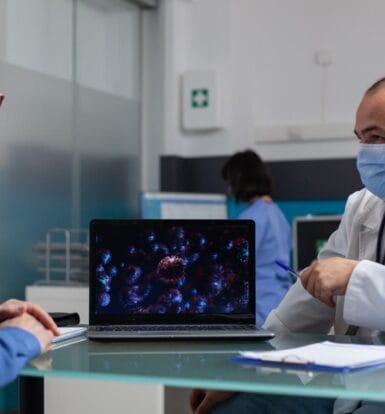 Doctor consulting an elderly patient with a laptop displaying medical data on the table in a modern clinic.