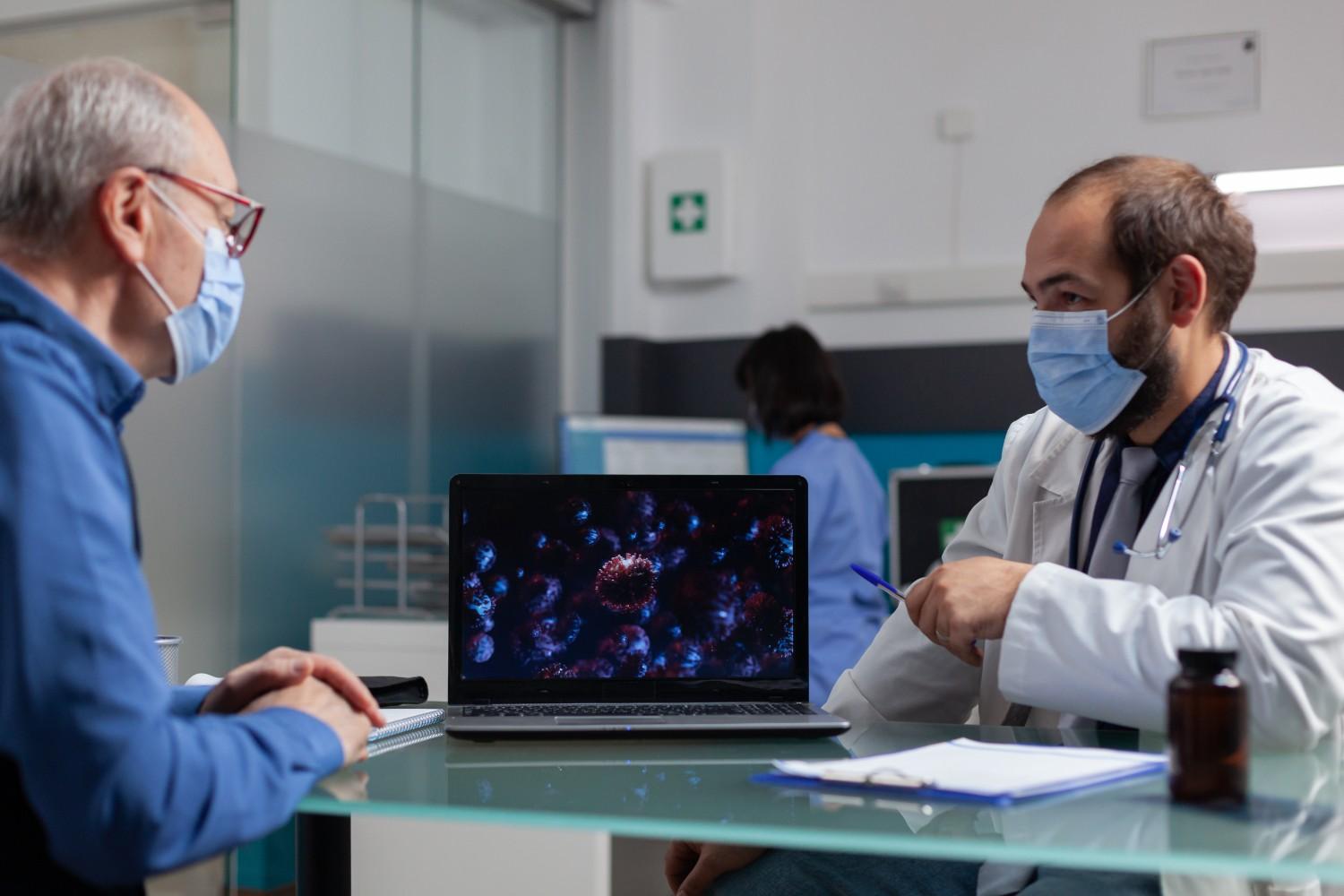 Doctor consulting an elderly patient with a laptop displaying medical data on the table in a modern clinic.