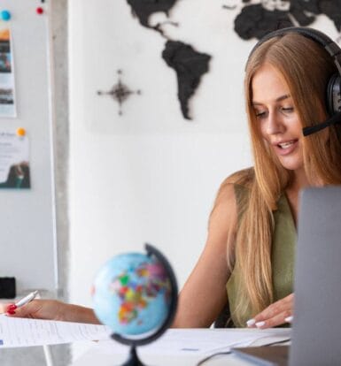 Virtual assistant in a headset working on healthcare administrative tasks at a desk with a laptop, map, and documents.