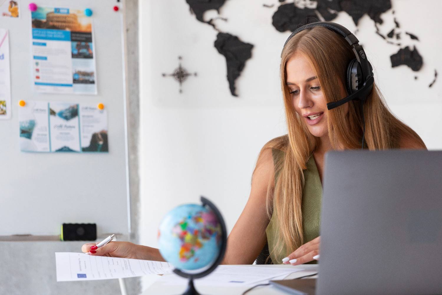 Virtual assistant in a headset working on healthcare administrative tasks at a desk with a laptop, map, and documents.