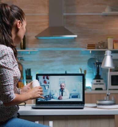 Patient consulting with a doctor via telemedicine on a laptop in a kitchen setting, showcasing the efficiency of virtual healthcare solutions.