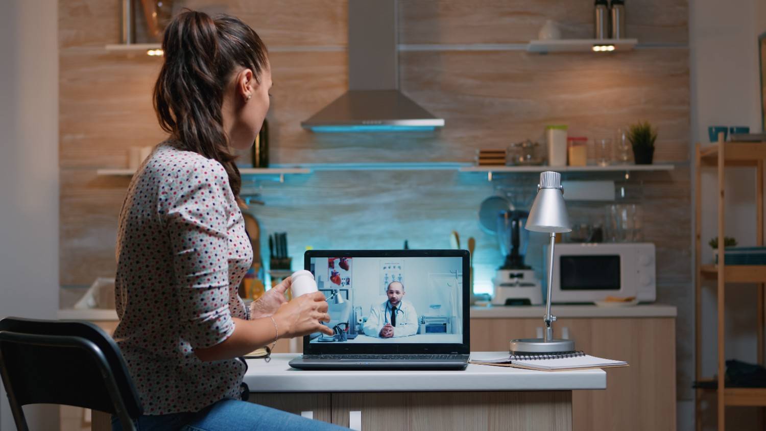 Patient consulting with a doctor via telemedicine on a laptop in a kitchen setting, showcasing the efficiency of virtual healthcare solutions.