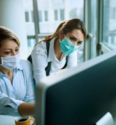 Two healthcare professionals wearing masks working on a computer, showcasing efficiency in a modern medical office.