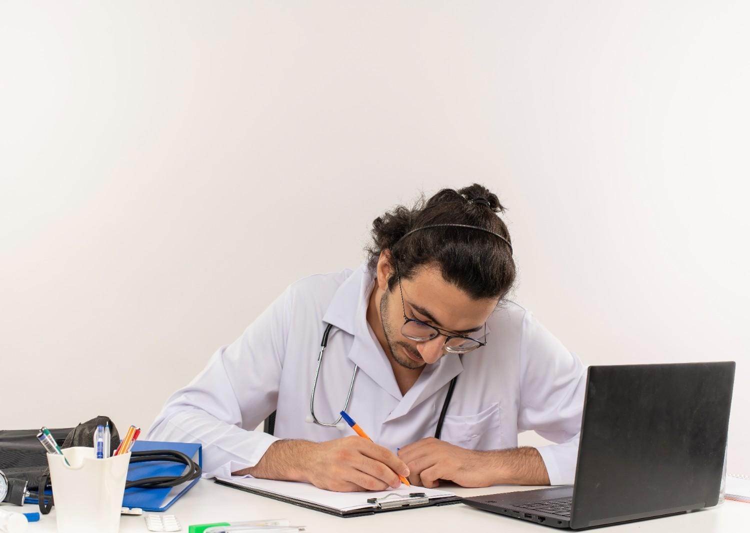 Doctor focusing on paperwork and documentation with a laptop on the desk, highlighting the challenges of medical documentation.