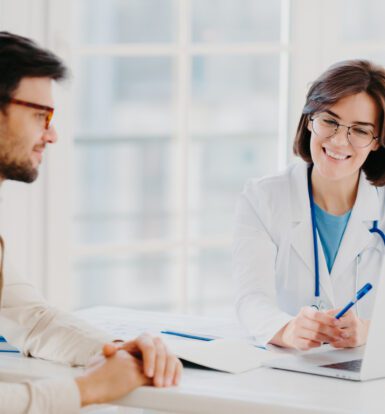 A doctor consulting with a patient while a virtual medical scribe records notes in the background.