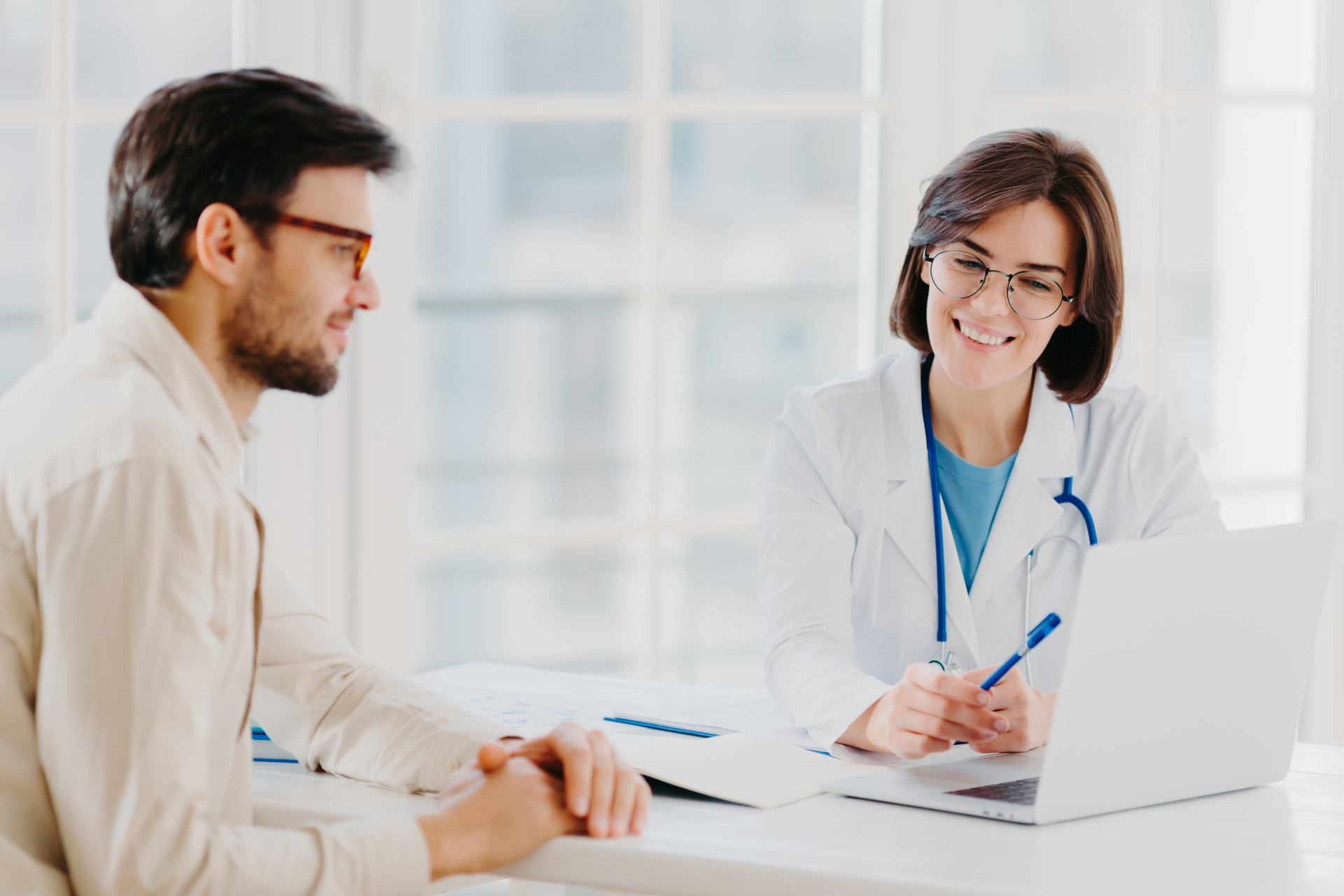 A doctor consulting with a patient while a virtual medical scribe records notes in the background.