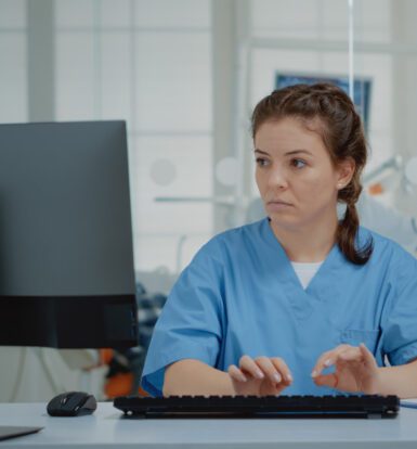 Medical coder working on a computer with ICD-10 book and AI-assisted coding software.