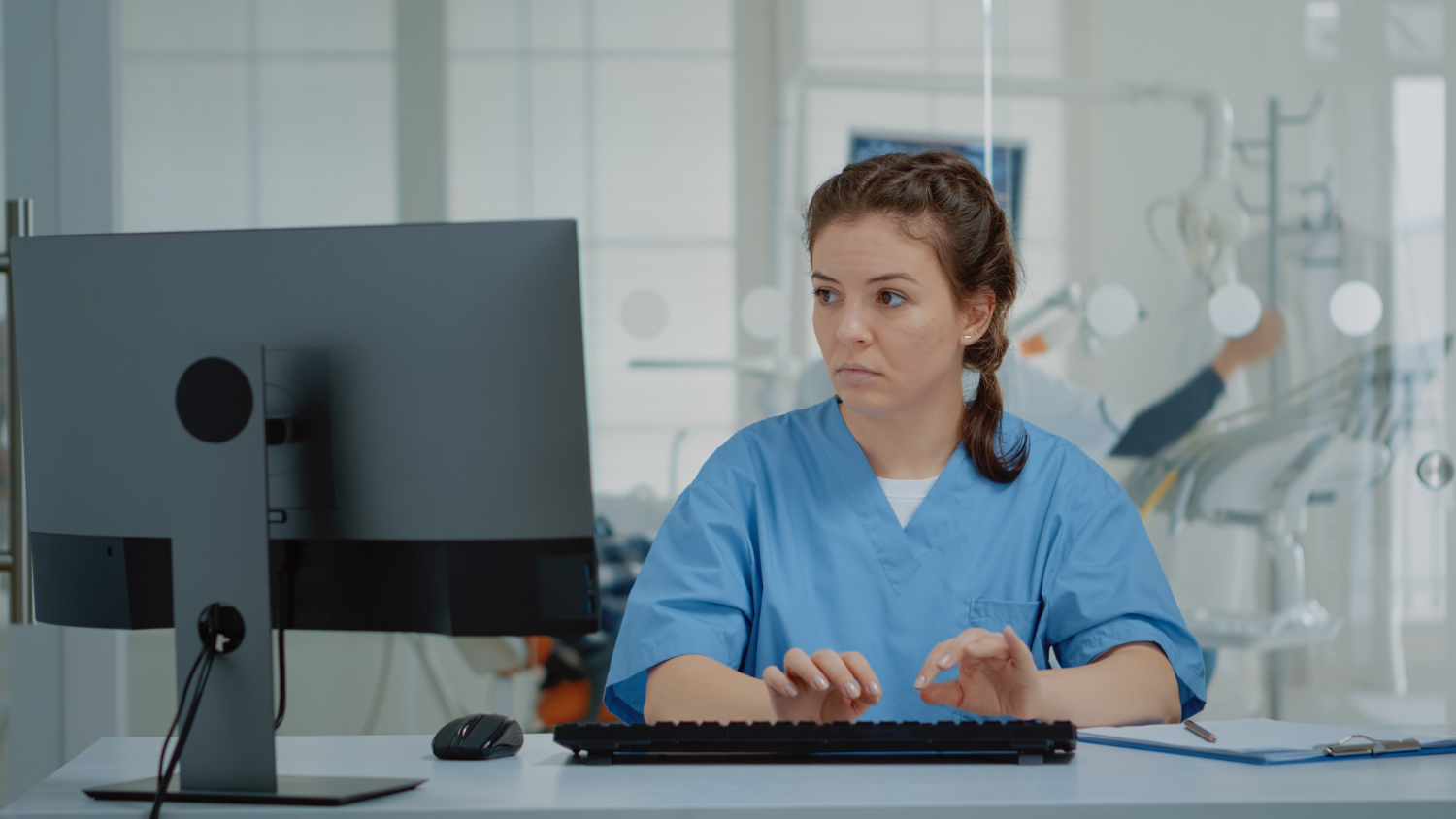 Medical coder working on a computer with ICD-10 book and AI-assisted coding software.