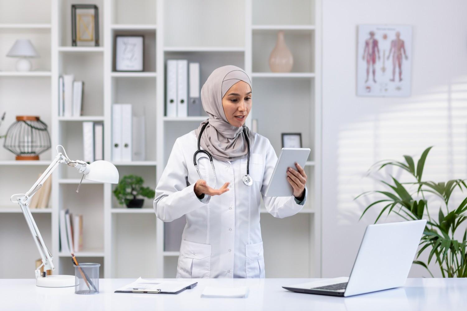 Female doctor in a modern medical office using a tablet for virtual patient consultation.