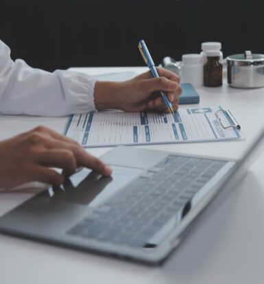 A healthcare professional filling out a prior authorization form while using a laptop for digital tracking and documentation.