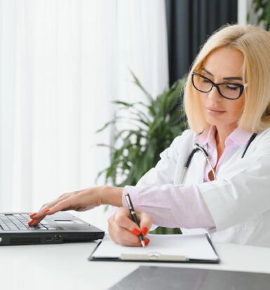 Doctor verifying insurance details on a laptop while taking notes.