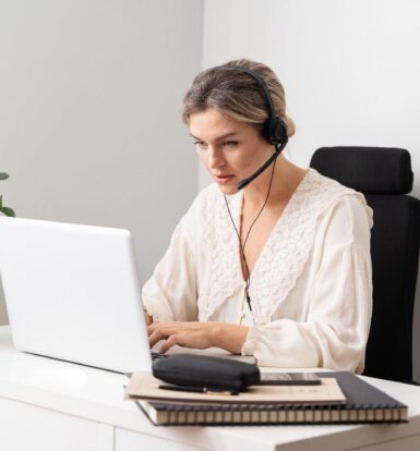 A woman with a headset working as a virtual medical receptionist at a laptop, managing patient calls and appointments in a healthcare setting.