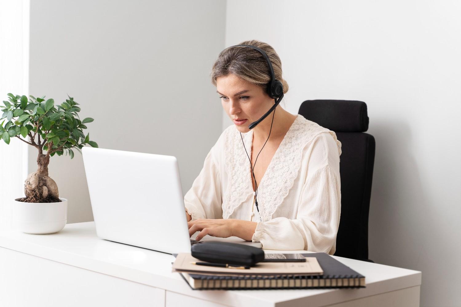 A woman with a headset working as a virtual medical receptionist at a laptop, managing patient calls and appointments in a healthcare setting.