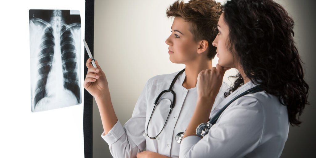 Two female doctors analyzing an X-ray image on a lightbox, discussing the results.