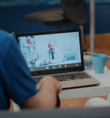 Virtual assistant for healthcare providers assisting a patient through a telemedicine consultation on a laptop screen.